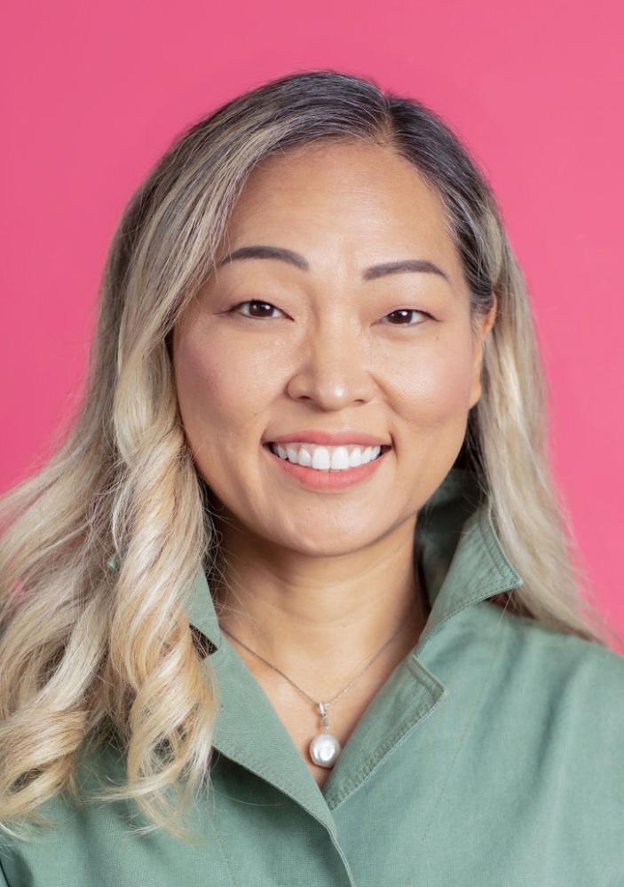 A smiling woman in a green shirt on a pink background.